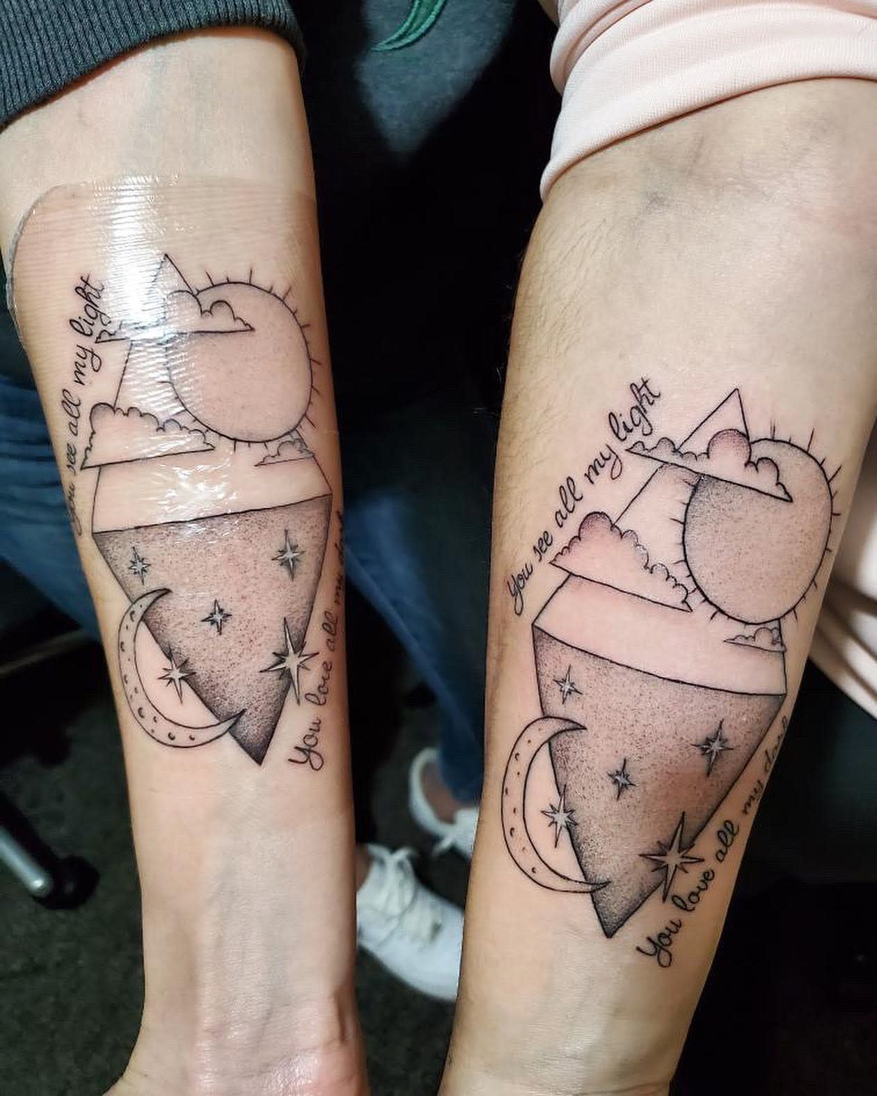 Two forearm tattoos featuring a sun, mountain, and moon with the phrase "You are all my light"